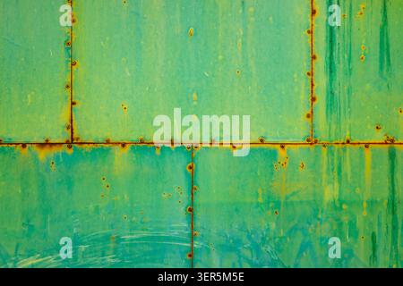 Close-up of a distressed green painted metal panel showcasing significant wear and rust. Visible seams and rivets highlight the industrial texture and Stock Photo