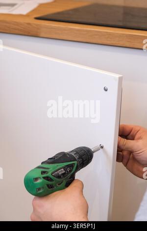 Person using cordless drill to attach white cabinet door in kitchen Stock Photo
