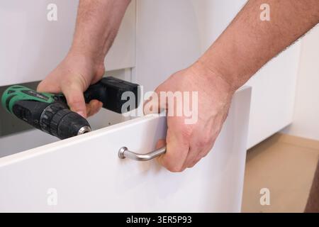 Man installing metal handle on white kitchen drawer Stock Photo