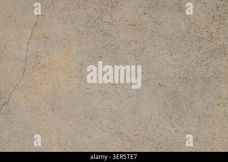 Close-up shot of a rough concrete wall surface featuring a subtle yellowish hue. A thin, dark crack runs diagonally, enhancing the aged and weathered Stock Photo
