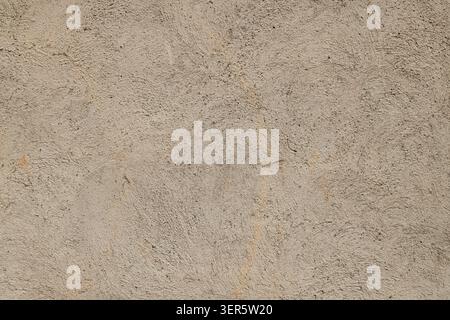 Close-up view of a rough textured concrete wall surface. Light beige color with swirling patterns and embedded aggregates creates a rugged appearance. Stock Photo