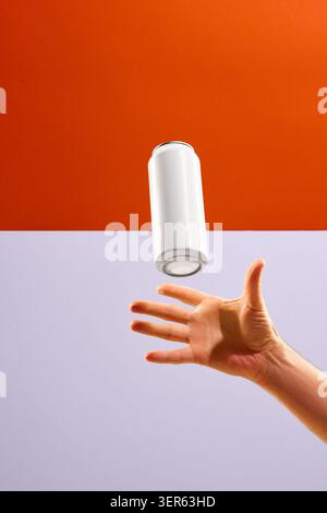 Blank white aluminum can floats above open hand on orange and lavender background with copy space. Stock Photo