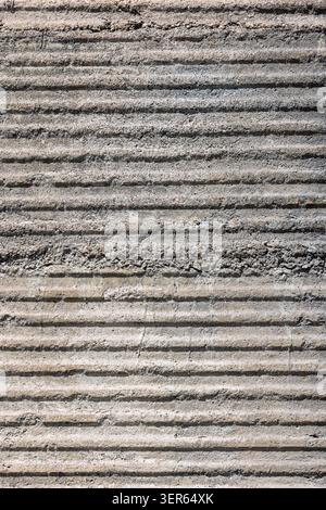 Close-up view of a textured concrete surface featuring prominent horizontal grooves. The weathered material showcases visible aggregate and subtle sha Stock Photo