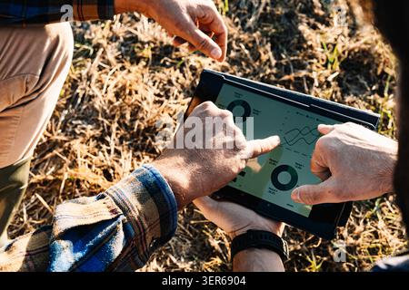 Farmers using a digital tablet are checking graphs about agricultural statistics in a mowed field Stock Photo