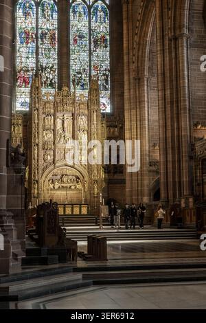 View of the ornate golden reredos and stained glass windows inside Liverpool Cathedral with people walking in the foreground Liverpool, England, Unite Stock Photo