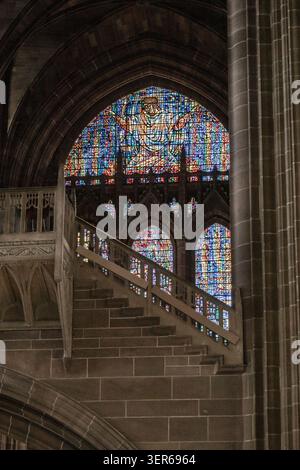 View of the intricate stained glass window and stone staircase inside the historic Liverpool Cathedral in Liverpool, England, United Kingdom. Stock Photo