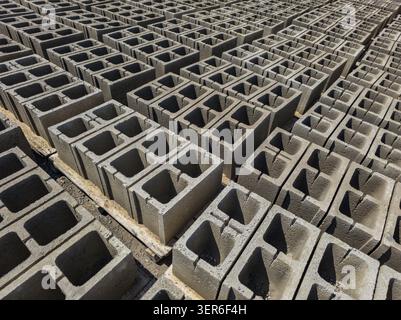 Rows of concrete cinder blocks arranged neatly on the ground. Batch manufactured building blocks are curing under direct sun. Stock Photo