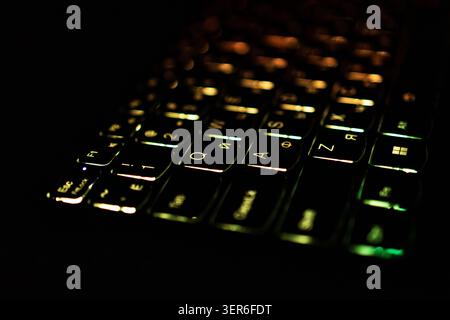 Low key macro of a backlit laptop keyboard glows with amber and green tones across reflective keycaps. Soft bokeh and selective focus create depth whi Stock Photo