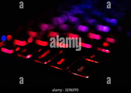 Low key macro of a backlit laptop keyboard surges with red and crimson around the Ctrl key. Intense glow and creamy bokeh heighten drama while the dia Stock Photo