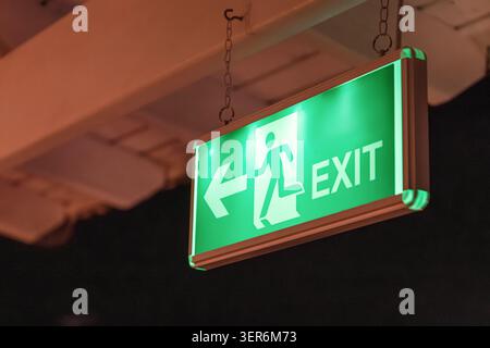 Green exit sign illuminating in the dark, showing an arrow and an emergency figure directing people to safety Stock Photo