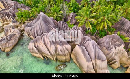 Stunning drone shot of exotic granite rock formations, lush palm trees, and crystal-clear turquoise ocean at the famous Anse Source d'Argent beach on Stock Photo