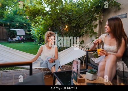 Women friends relaxing in backyard hammock drinking beverages Stock Photo