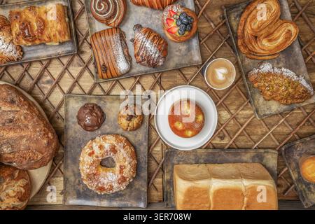 An assortment of croissants, danishes, cookies and breads arranged on metal trays over a rustic wooden lattice table. Stock Photo