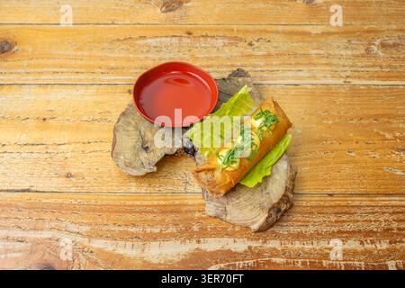 A woven bamboo tray displays a row of Vietnamese spring rolls, with a small container of fish sauce and wooden chopsticks resting on the edge of the p Stock Photo