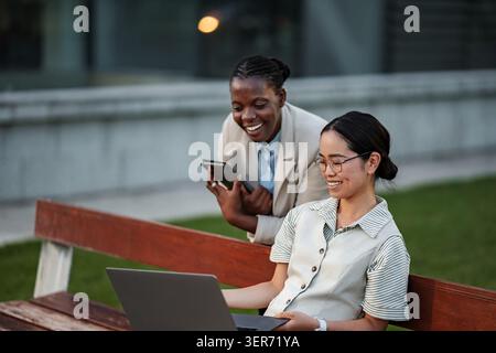 Diverse women collaborating on laptop and mobile device Stock Photo