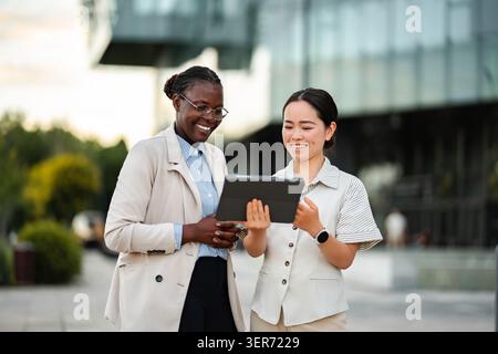 Diverse businesswomen collaborating using digital tablet outside office Stock Photo