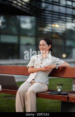 Professional woman smiling outdoors working on bench with laptop Stock Photo