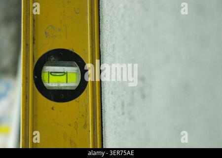A worker uses a leveling tool to ensure a wall fixture is straight. The bubble is centered inside the level. This is part of the construction process Stock Photo