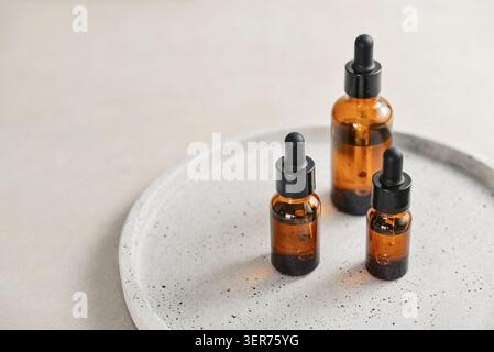 Natural skincare and beauty treatment concept with amber glass cosmetic containers arranged on a round tray. Three dropper bottles filled with clear l Stock Photo