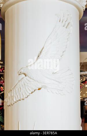 Close-up view of an exquisite white plaster bas-relief depicting a majestic flying eagle with intricately carved feathers and outstretched wings on a Stock Photo