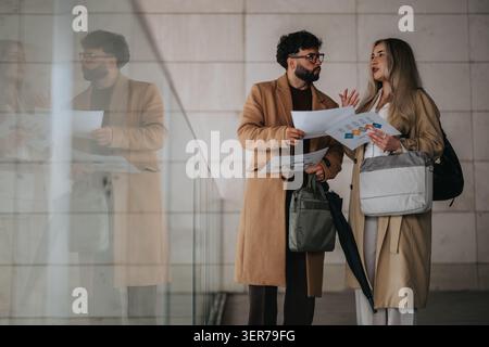 Two professionals discussing business documents in a modern glass-lined office corridor Stock Photo