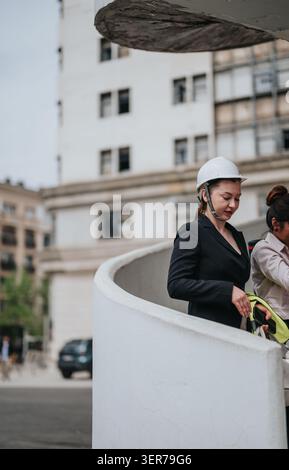 Female project manager in hard hat inspecting urban construction site while holding safety vest Stock Photo