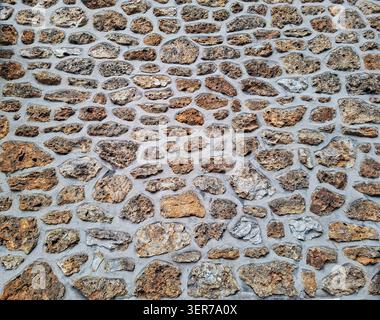 The view shows a wall built with various natural stones that are placed in grey mortar. This wall showcases a rustic style typical of Mediterranean ar Stock Photo