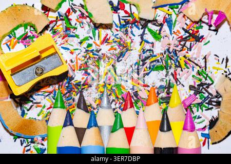 Colored pencils with yellow sharpener, wooden shavings and colorful graphite crumbs on white background Stock Photo