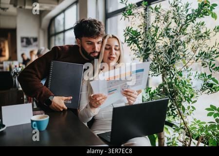 Business partners reviewing charts and reports on a laptop while working together in a cozy cafe Stock Photo