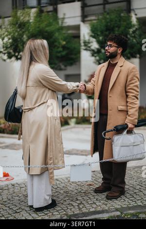Business colleagues shaking hands outdoors in professional coats during urban meeting Stock Photo