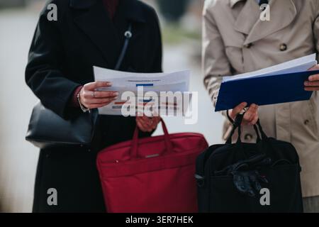 Two business colleagues reviewing documents and charts while standing with briefcases outdoors Stock Photo