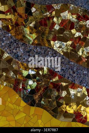 Abstract mosaic art featuring irregular pieces of gold and reddish glass, interspersed with bands of small, gray pebbles, in Herrenhausen Gardens. Stock Photo