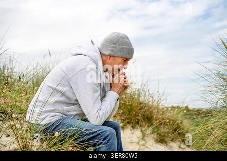 A mature man sitting alone deep in thought, outdoors at the beach Stock Photo