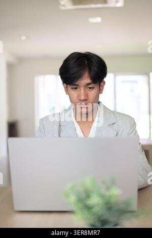 Authentic vertical lifestyle portrait of a young non-binary Thai Isan professional or student looking down at a computer screen with a focused express Stock Photo
