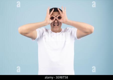 Funny young man making glasses with hands over his eyes looking forward Stock Photo