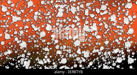 Abstract background featuring a dense pattern of white, textured, circular particles layered over a vibrant orange and dark gradient backdrop. Stock Photo