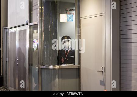 Tokyo, Japan - 25 January 2026: View of a security guard wearing a uniform and face mask standing inside a glass booth at the QFRONT building in Shibu Stock Photo
