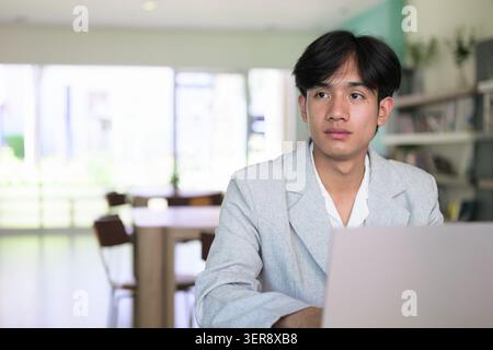 Authentic horizontal lifestyle portrait of a young non-binary Thai Isan professional or student looking away with a serious expression. Thinking or pl Stock Photo