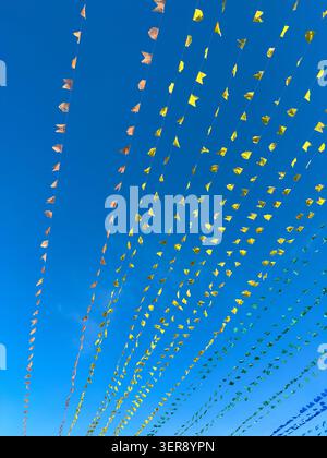 Brightly colored small triangular flags stretch across clear blue sky on strings. Natural light illuminates the celebratory decorations, suggesting ou Stock Photo