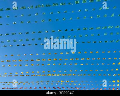 Rows of colorful small flags strung on wires against clear blue sky. Festive decoration, bright colors, clean vibrant background. Suitable for party, Stock Photo
