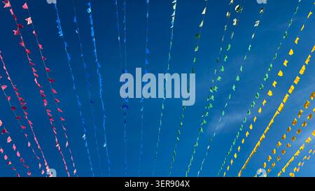 Brightly colored paper flags strung on thin lines against clear blue sky. Festive decoration suggests celebration, tradition, or community gathering. Stock Photo