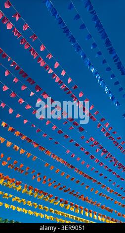 Jagged fabric flags in rows of red, orange, blue, and yellow stretch across vibrant blue sky. Clear lighting accentuates textures, creating festive at Stock Photo