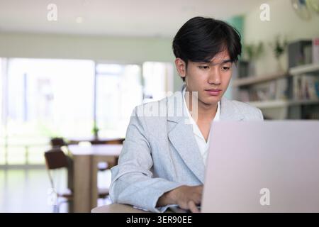 Authentic horizontal lifestyle portrait of a young non-binary Thai Isan professional or student looking down at a computer screen with a focused expre Stock Photo