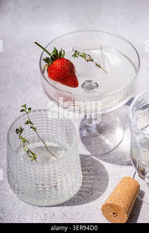 Elegant summer champagne cocktail in a textured coupe glass, garnished with fresh strawberry and thyme. Minimal bright scene with glassware and cork, Stock Photo