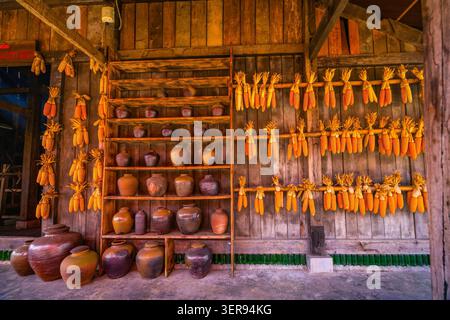 Rows of dried corn cobs hang on a rustic wooden wall beside clay jars and shelves in a village home near Sapa, with Fansipan mountain region culture a Stock Photo