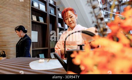 Traditional Japanese matcha tea ceremony in Tokyo, featuring a kimono-clad woman preparing tea beside a cast iron kettle, with calm interior and autum Stock Photo