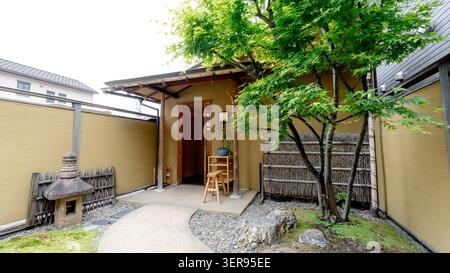 Peaceful entrance of a Japanese restaurant in Tokyo, featuring a small garden courtyard with maple tree, stone lantern, bamboo fence, and traditional Stock Photo