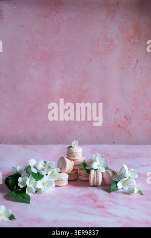 Pink macarons filled with pistachio cream arranged on a soft pink backdrop, decorated with delicate white flowers and green leaves for an elegant spri Stock Photo