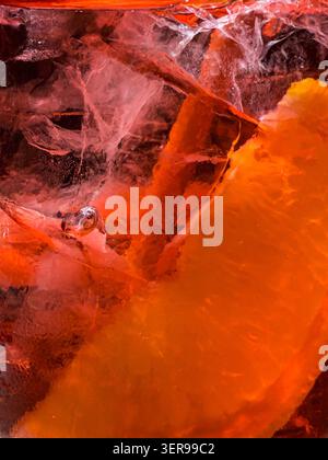 Vibrant macro close-up of a fresh Aperol cocktail with sparkling bubbles, large ice cubes and a citrus slice. Abstract orange background, chilled summ Stock Photo