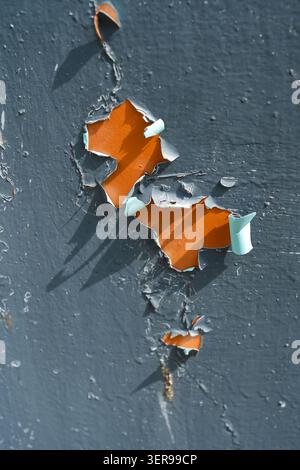 A close-up image of peeling paint on a weathered surface, revealing a contrasting bright orange backdrop beneath. The texture creates an artistic abst Stock Photo